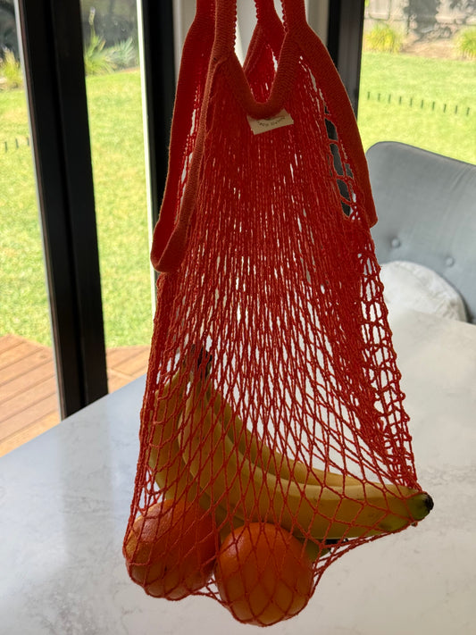 Orange cotton net shopping bag holding bananas and oranges, on our kitchen bench in Bayside